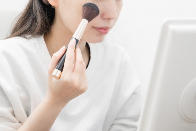 メイクブラシを頬にあてる女性の上半身アップ