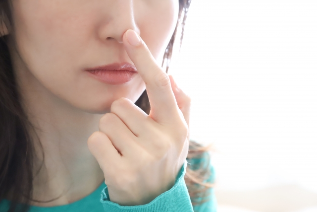 人差し指で鼻先を触る女性の頬から鎖骨のアップ
