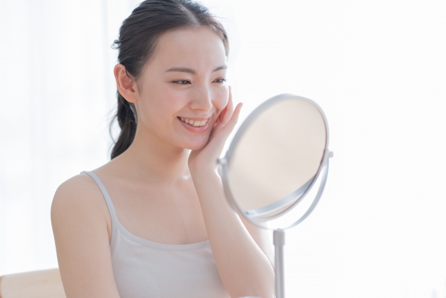 置き鏡の前で頬に手を当てる笑顔の女性